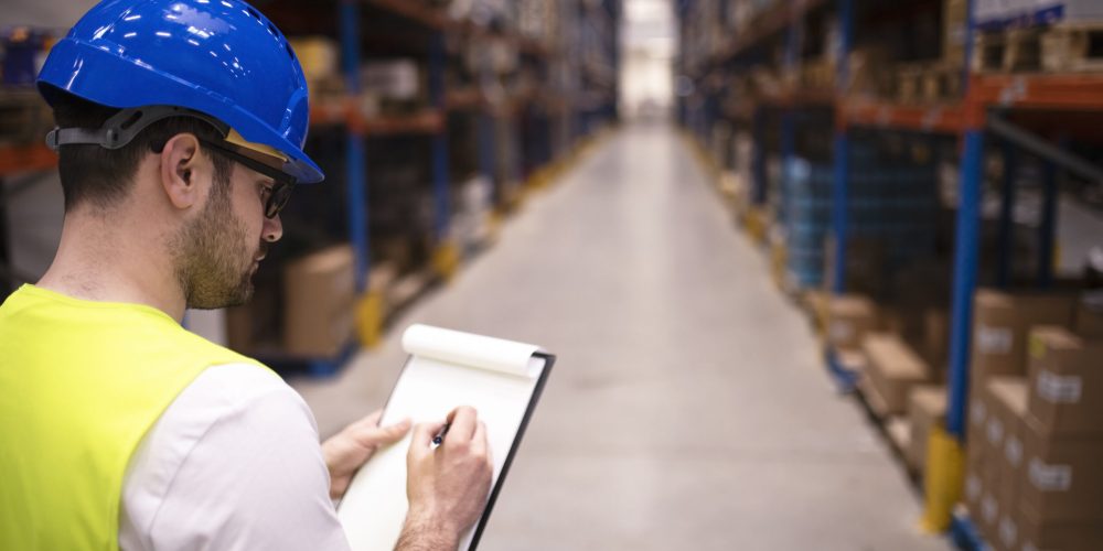 Factory worker holding clipboard and checking inventory of warehouse storage department.